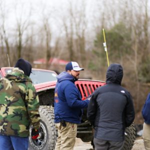 Four people standing around a dirty jeep