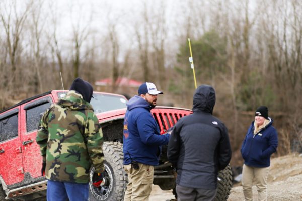 Four people standing around a dirty jeep