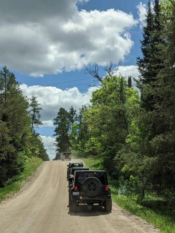 Line of 4-wheel-drive vehicles on a dirt road with lots of trees